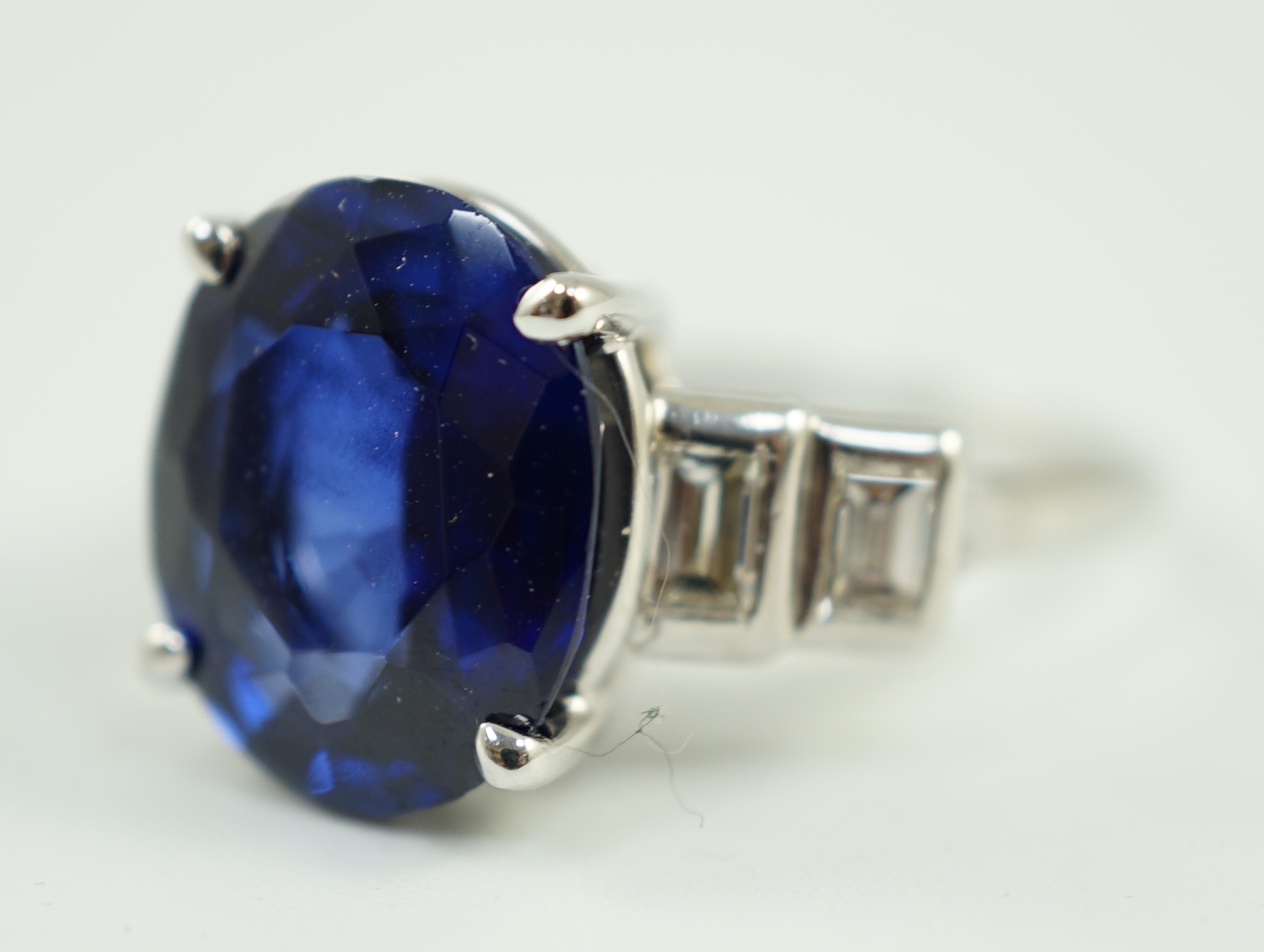 A platinum and single stone oval cut sapphire set cocktail ring, with graduated four stone baguette cut diamond set shoulders